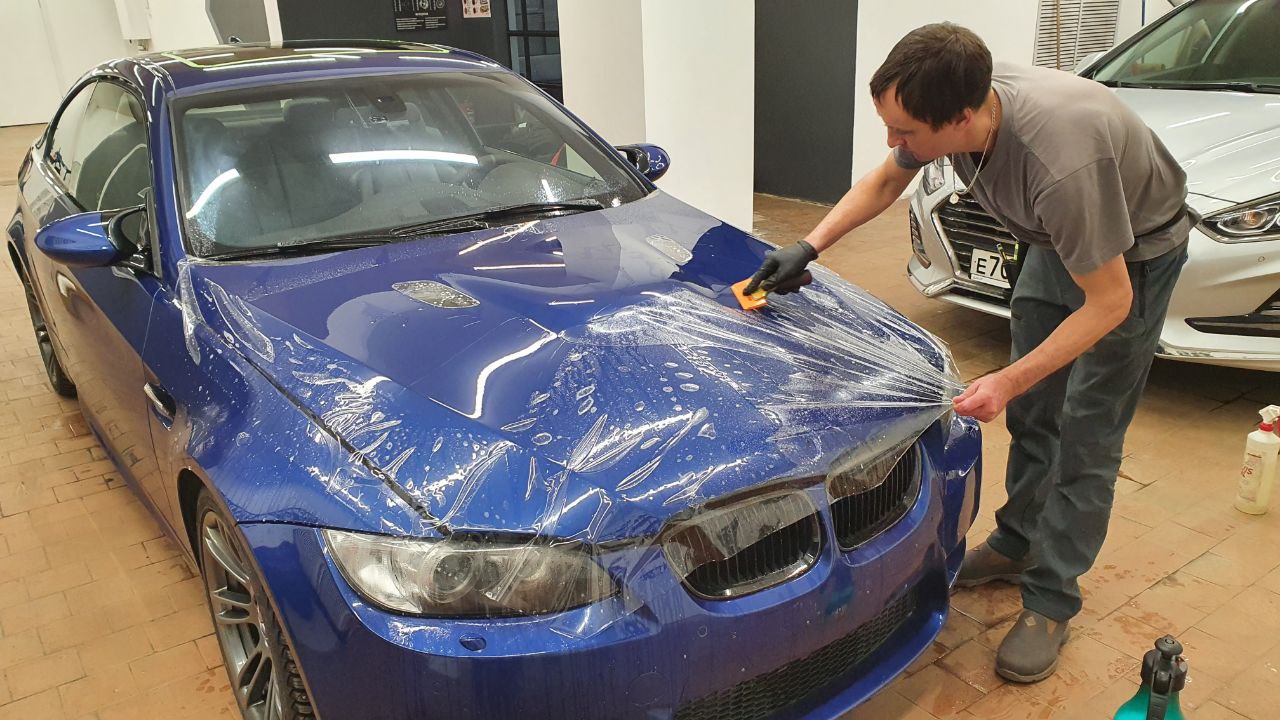 Мастер укладывает защитную плёнку на капот BMW